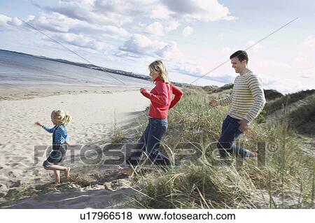 Stock Photo - Parents and daughter (5-6) running onto beach. Fotosearch