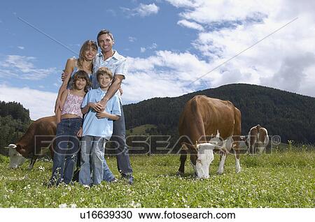 Stock Image - Parents with children (7-9) embracing in field with cows, portrait. Fotosearch