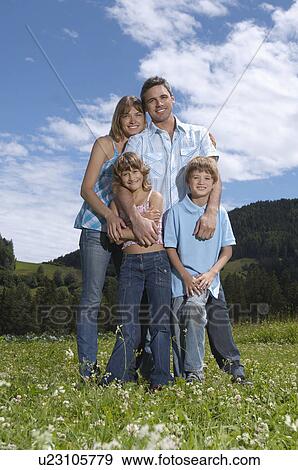 Stock Photo - Parents with children (7-9) embracing in field, portrait. Fotosearch