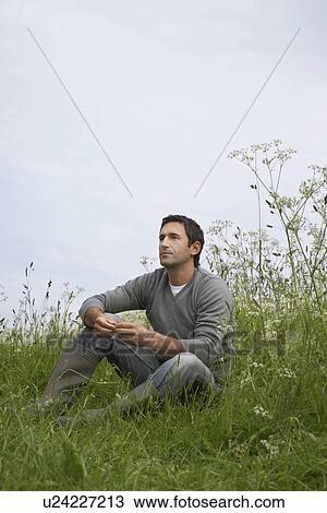 Stock Image - Pensive man sitting in field. Fotosearch