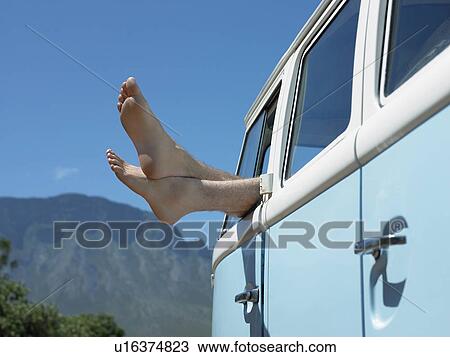 Stock Image - Person in parked camper van, feet sticking out of window, close up. Fotosearch