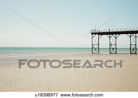 Stock Photo - Pier stands on beach at low tide. Fotosearch