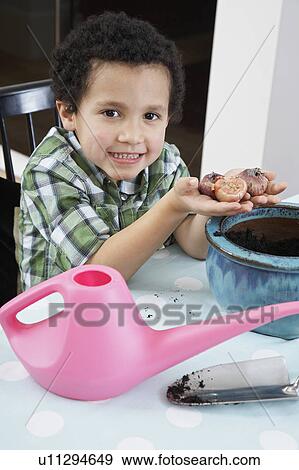 Stock Photo - Portrait of boy (5-6) holding flower bulbs, smiling. Fotosearch