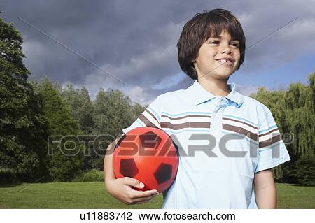 Stock Image - Portrait of boy (7-9) in meadow with football, looking away. Fotosearch