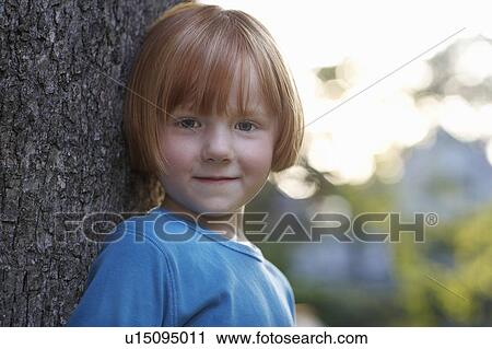 Stock Image - Portrait of girl (5-6) leaning against tree. Fotosearch