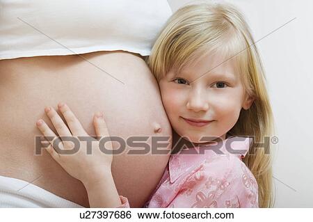 Stock Photograph - Portrait of girl (7-9) hugging pregnant mother's belly. Fotosearch