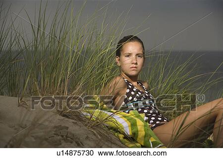 Stock Image - Portrait of girl on sand dune with sea in background. Fotosearch