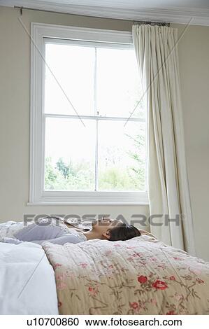 Stock Image - Portrait of young woman lying on bed. Fotosearch