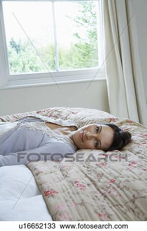 Portrait of young woman lying on bed, smiling View Large Photo Image Stock Image - Portrait of young woman lying on bed, smiling. Fotosearch