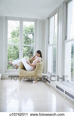 Stock Image - Portrait of young woman relaxing in armchair at porch. Fotosearch