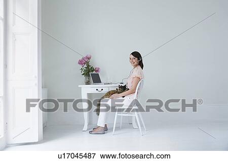 Portrait of young woman sitting by desk with cat View Large Photo Image Stock Photo - Portrait of young woman sitting by desk with cat. Fotosearch