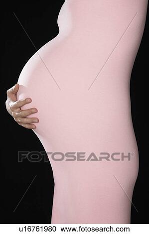 Pregnant woman in body suit holding abdomen, mid section, side view, studio shot View Large Photo Image Stock Image - Pregnant woman in body suit holding abdomen, mid section, side view, studio shot. Fotosearch