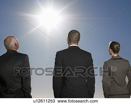 Rear view of three business people in suits looking up at the sun for inspiration View Large Photo Image Stock Image - Rear view of three business people in suits looking up at the sun for inspiration. Fotosearch