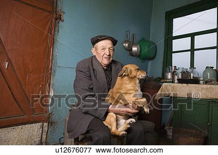 Stock Photo - Russia, senior man and dog in kitchen. Fotosearch