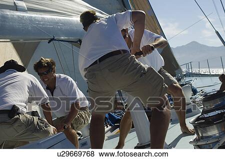 Stock Photo - Sailors working on windlass on yacht. Fotosearch