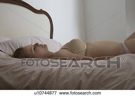 Stock Photo - Semi-dress woman resting on bed. Fotosearch