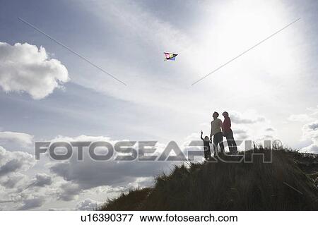 Stock Photo - Silhouette of parents and child flying kite on dunes. Fotosearch