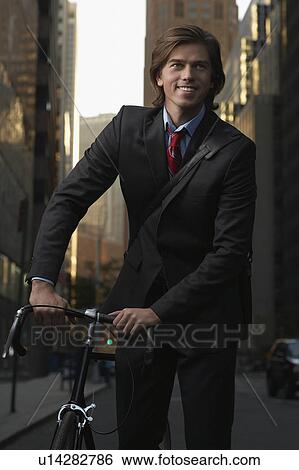 Stock Photograph - Smiling man standing by bicycle in street, portrait. Fotosearch