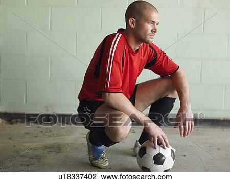 Stock Image - Soccer player crouching with ball, side view. Fotosearch