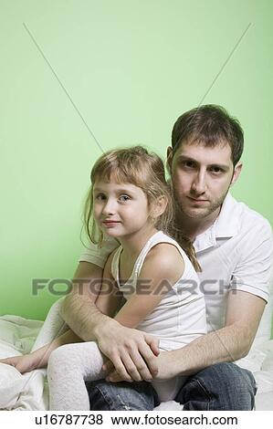 Studio shot of girl (7-9) sitting on bed with father View Large Photo Image Stock Photo - Studio shot of girl (7-9) sitting on bed with father. Fotosearch