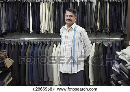 Stock Photo - Tailor standing in shop in front of clothes racks, portrait. Fotosearch