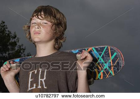 Stock Photo - Teenage boy (13-15) holding skateboard, outdoors, portrait, low angle view. Fotosearch