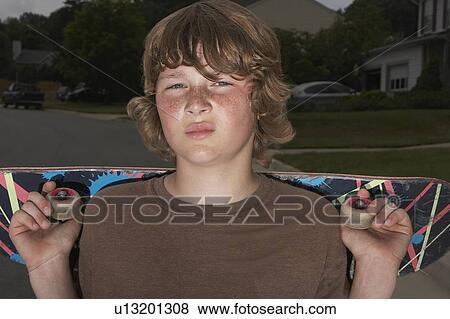 Stock Photo - Teenage boy (13-15) holding skateboard standing on street, portrait, close up. Fotosearch