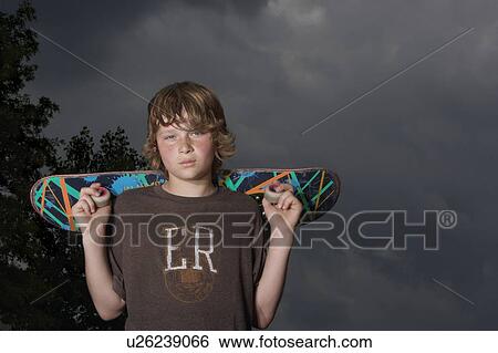 Stock Photograph - Teenage boy (13-15) holding skateboard, outdoors, portrait, low angle view. Fotosearch