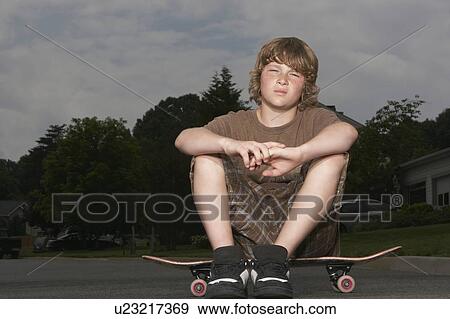 Teenage boy (13-15) sitting on skateboard on street, portrait View Large Photo Image Stock Photo - Teenage boy (13-15) sitting on skateboard on street, portrait. Fotosearch