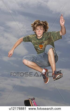 Teenage boy (16-17) jumping on skateboard on street, low angle view View Large Photo Image Stock Image - Teenage boy (16-17) jumping on skateboard on street, low angle view. Fotosearch