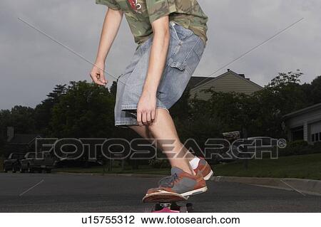 Stock Image - Teenage boy (16-17) skateboarding on street, low section. Fotosearch