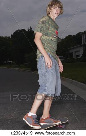 Stock Photo - Teenage boy (16-17) skateboarding on street, portrait. Fotosearch