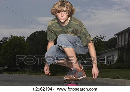 Stock Photo - Teenage boy (16-17) skateboarding on street, portrait. Fotosearch