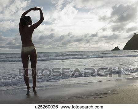 Stock Photograph - Thailand, young woman in bikini, stretching on beach. Fotosearch