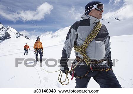 Stock Photo - Three hikers joined by safety line in snowy mountains. Fotosearch