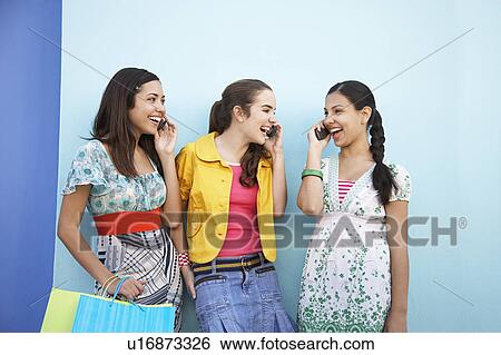 Stock Photograph - Three teenage girls (16-17) using mobile phones standing in front of blue wall. Fotosearch