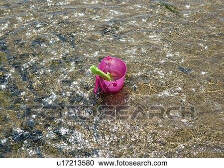 Stock Image - Toy bucket and spade in shallow water. Fotosearch
