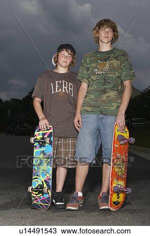 Stock Image - Two adolescent boys (13-17) with skateboards standing outdoors, portrait. Fotosearch