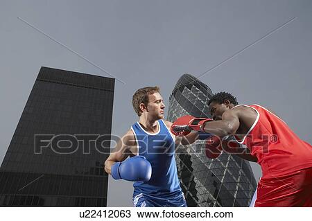Stock Image - Two boxers fighting amongst downtown buildings, low angle view, London, England. Fotosearch