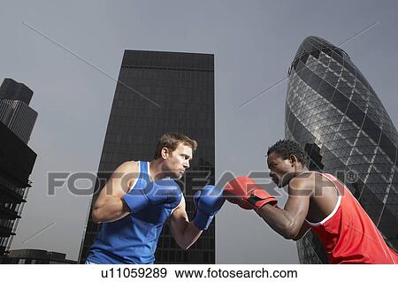 Stock Photo - Two boxers punching amongst downtown buildings, low angle view, London, England. Fotosearch