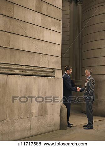 Stock Photo - Two businessmen shaking hands at entrance of monumental building. Fotosearch