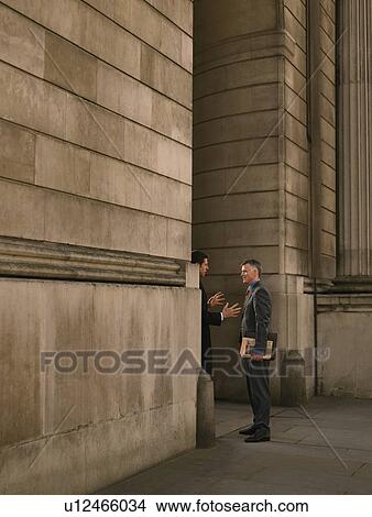 Picture - Two businessmen talking at entrance of monumental building. Fotosearch