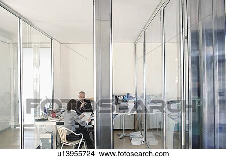 Two businesspeople sitting in office, having meeting, elevated view. View Large Photo Image Picture - Two businesspeople sitting in office, having meeting, elevated view.. Fotosearch