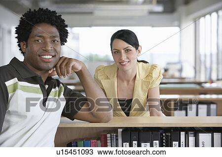 Stock Image - Two colleagues sitting in office, smiling, portrait. Fotosearch
