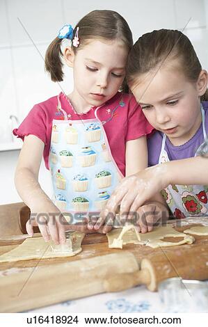 Picture - Two girls (5-6) cutting dough in kitchen. Fotosearch