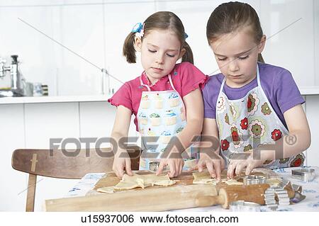 Stock Photograph - Two girls (5-6) cutting dough in kitchen. Fotosearch