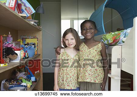 Two girls (6-7) standing in room, portrait View Large Photo Image Stock Photography - Two girls (6-7) standing in room, portrait. Fotosearch