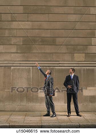 Stock Photography - Two men on sidewalk, looking up. Fotosearch