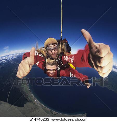Stock Image - Two skydivers giving thumbs-up in mid-air, portrait. Fotosearch