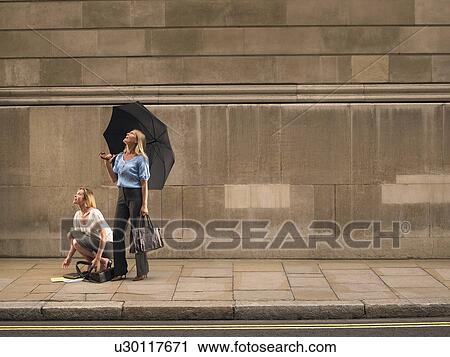 Stock Image - Two women on sidewalk, looking up. Fotosearch